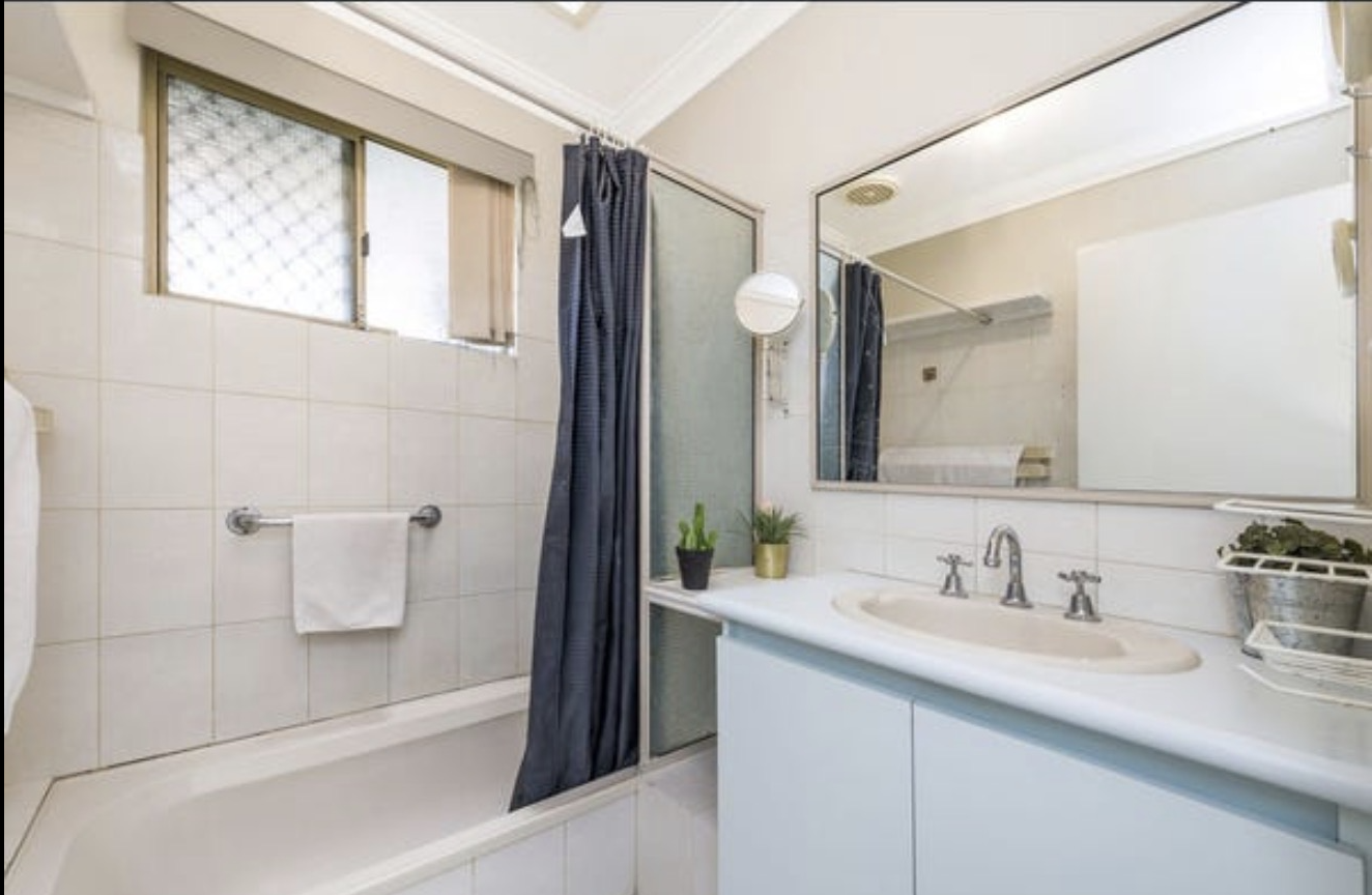 Bathroom before renovation in Perth — dated bath with shower curtain, small tiles and old vanity