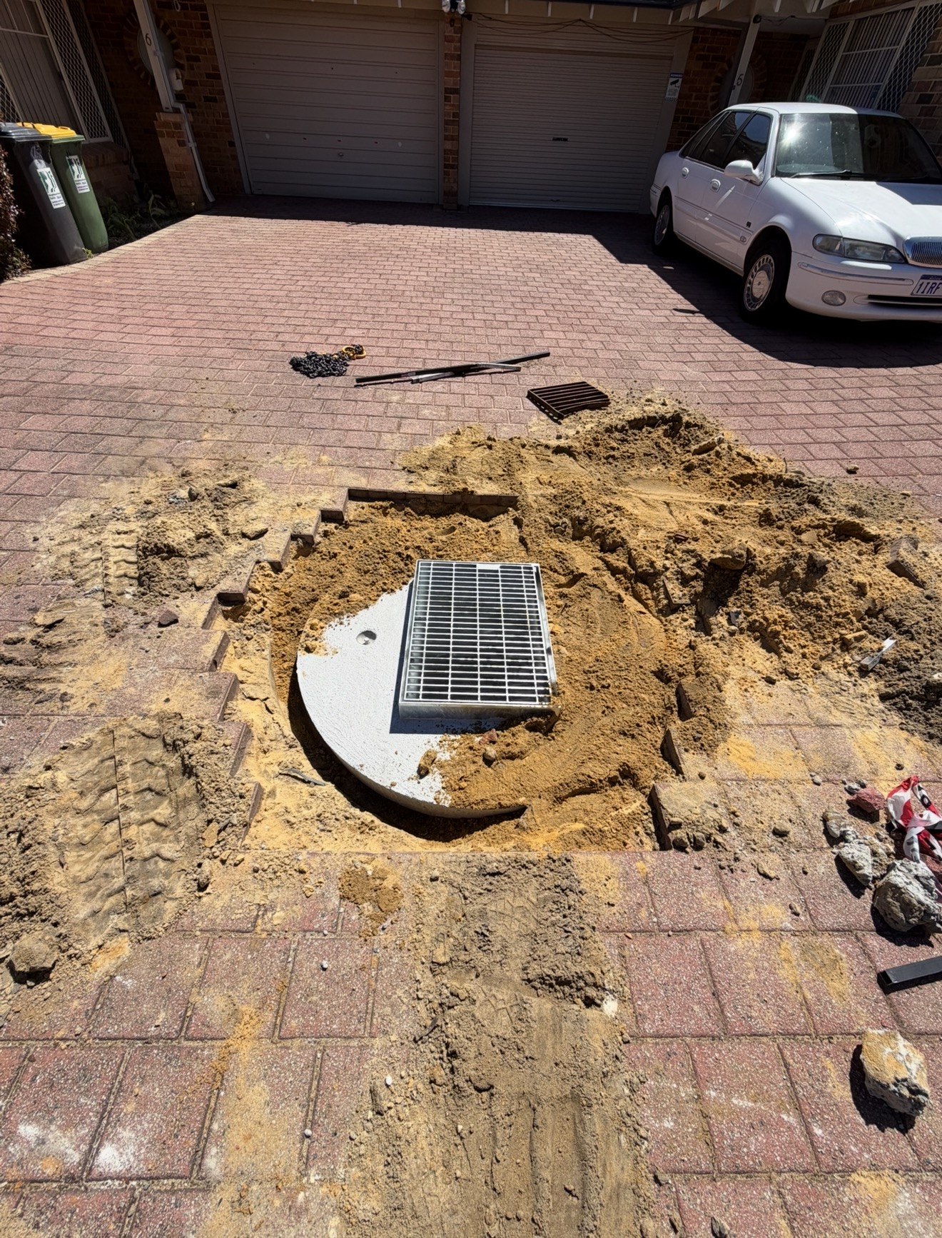 Soakwell lid replacement underway on a paved driveway in Perth — old lid excavated and a new heavy-duty grate ready to install